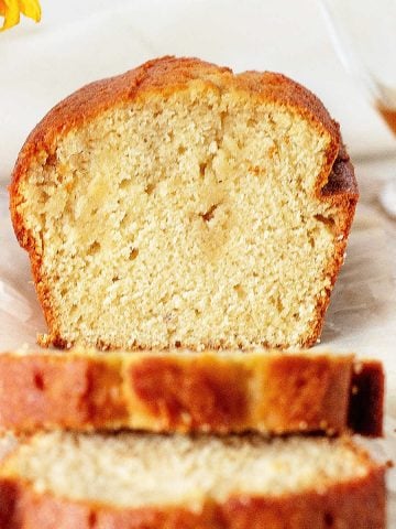 Close up image of cut loaf cake with slices on white paper on a white surface.