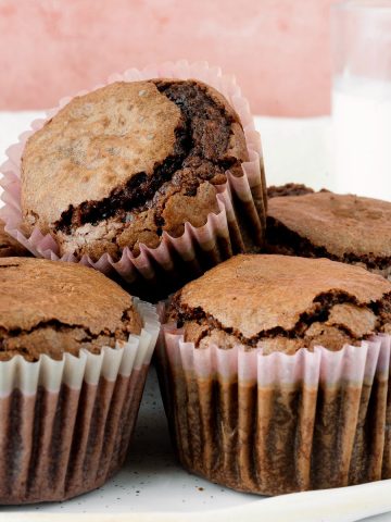 Small pile of brownie muffins in paper liner with a pink background.
