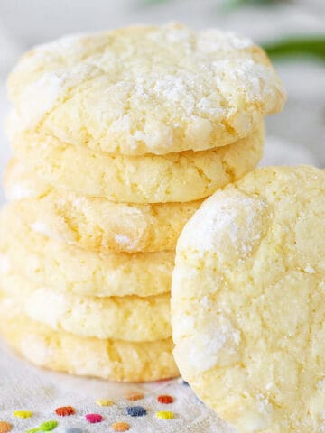 Several lemon crinkle cookies stacked on a white napkin with colored dots.