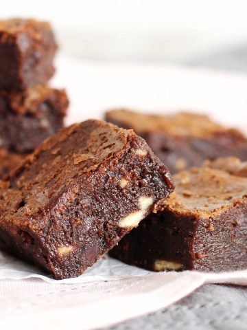 Fudgy triple chocolate brownies leaning on each other on a light pink cloth. White background.