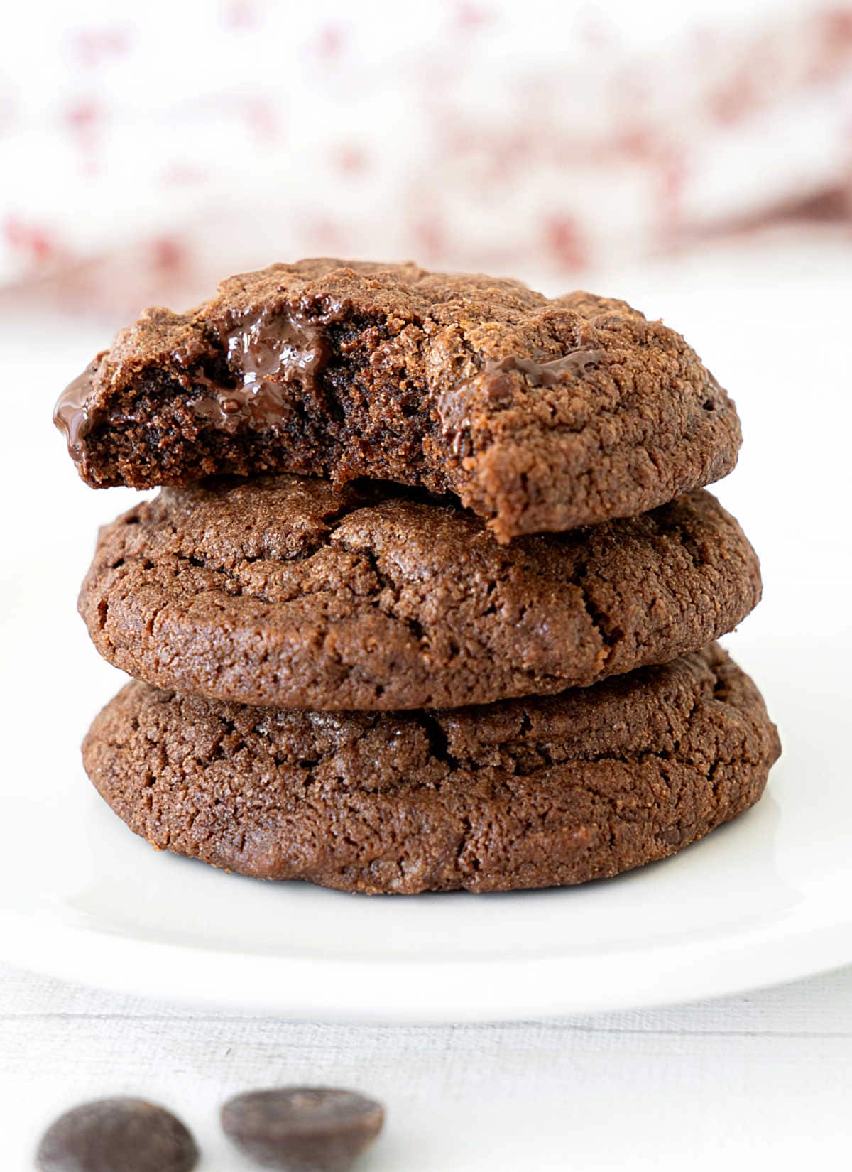 Stack of three chocolate cookies on a white plate. Top one is bitten.